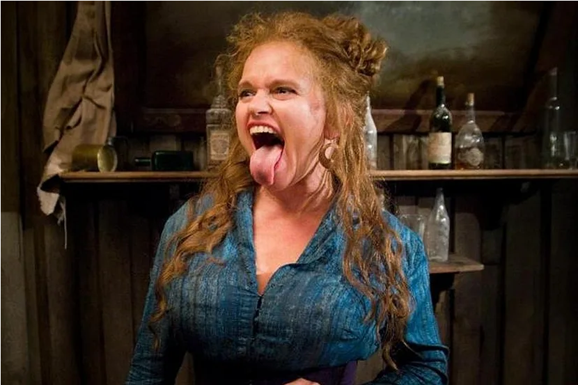 zdjęcie: kobieta wystawiająca język na tle półki z kilkoma szklanymi butelkami